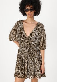 Abito con stampa leopardo in marrone e beige, con scollatura a V profonda, maniche a sbuffo corte e vita smock. Abbinato a occhiali da sole rettangolari.