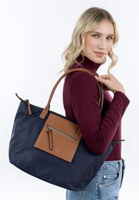 Navyblauwe tas met bruine leren accenten, ritsvak en twee schouderbanden. Gladde textuur met contrasterende materialen.
