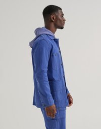 Blue corduroy jacket with large front pockets, button closure, and matching pants. Features a lavender hooded sweatshirt layered underneath.