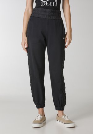 Zwarte joggers met een gestructureerde elastische tailleband, taps toelopende boorden en zijaccenten. Gemaakt van zachte stof, geschikt voor casual draagstijl.