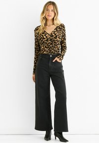 Leopard print long-sleeve top with a V-neck and fitted design paired with high-waisted wide-leg black jeans and black heeled boots.