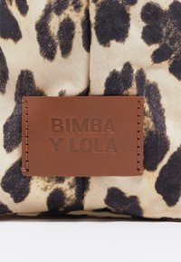 Beżowa tkanina z czarnymi plamami w stylu lamparta ma brązową skórzaną metkę wytłoczoną z napisem "BIMBA Y LOLA". Gładka faktura, prosty design.