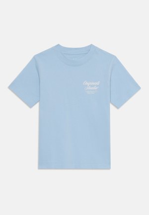 T-shirt de algodão azul claro com mangas curtas, decote redondo e um pequeno logótipo gráfico branco na área do peito esquerdo. Textura suave.