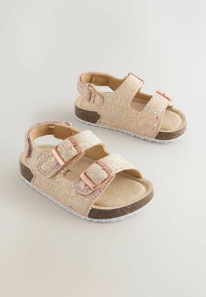 Ble ščeče rožnate sandale z dvema nastavljivima trakoma, zlatimi zaponkami, rjavimi vložki in belimi gumijastimi podplati s teksturirano, bleščečo površino.