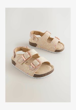 Sandales roses scintillantes avec deux brides réglables, boucles dorées, semelles intérieures beiges et semelles extérieures blanches en caoutchouc, présentant une finition texturée et étincelante.