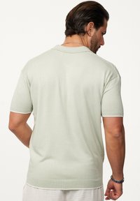 Polo-Shirt in Hellgrün, mit kurzen Ärmeln, Stricktextur, traditionellem Kragen und einem klaren, schlichten Design ohne sichtbare Logos oder Muster.