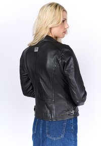 Svart läderjacka med en figurnära design, som har en logotypetikett på baksidan, vinklade sömmar och spännelement vid midjan.