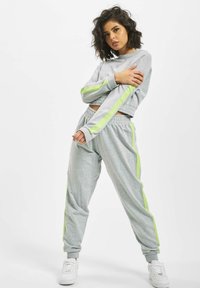 Gray cropped sweatshirt and matching joggers with neon green side stripes, made from a soft material. White sneakers complete the outfit.