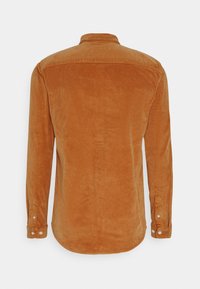 Camisa de pana marrón con cuello abotonado, mangas largas y botones blancos. Presenta una textura acanalada vertical y un dobladillo curvo.