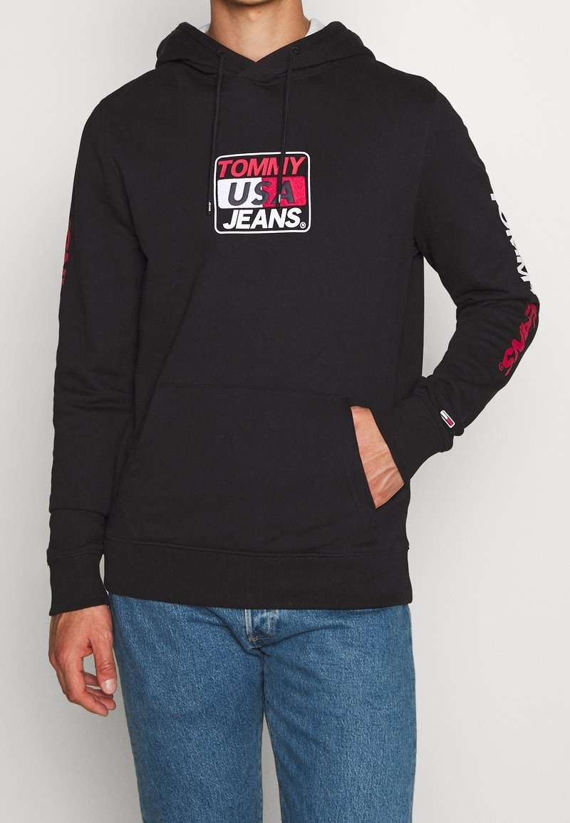 Zwarte hoodie van een katoenmix, met een voork pocket, een capuchon met trekkoord en een gedurfde "TOMMY USA JEANS" logo in wit en roze.