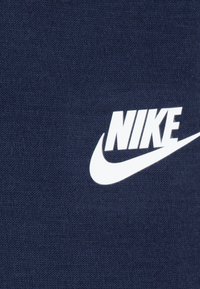 Tissu bleu marine avec une finition texturée présentant un logo Nike blanc et une virgule bien visible. Design simple et classique.