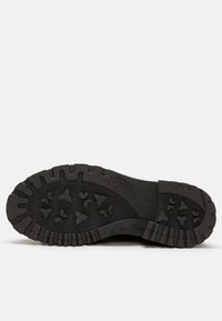 Suela de zapato de goma negra con una superficie texturizada, que presenta patrones de tracción en forma de triángulo y corazón para mayor agarre y estabilidad.