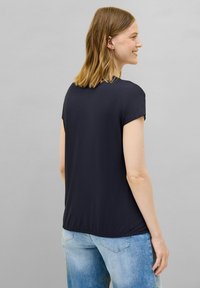 Top corto de color azul marino oscuro con un escote redondeado, que presenta una textura suave y un ajuste relajado, combinado con jeans de color azul claro.