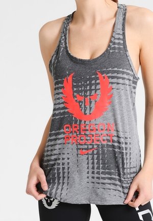 Personne portant un débardeur sportif gris avec le logo rouge de l'Oregon Project et un motif géométrique, tenant l'ourlet avec les deux mains.