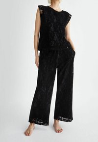 Set bicolore in pizzo nero composto da un top senza maniche con design testurizzato e pantaloni a gamba larga con rifiniture in pizzo. Tessuto morbido, vestibilità comoda.