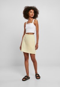 Falda amarilla de longitud a la rodilla con cinturilla elástica, combinada con un top corto blanco. Chanclas negras completan el atuendo.