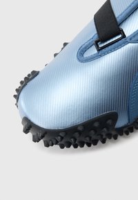 Jasnoniebieski but sportowy o błyszczącym, teksturowanym wykończeniu, z czarnym paskiem i wytrzymałą czarną gumową podeszwą z wystającymi kolcami.