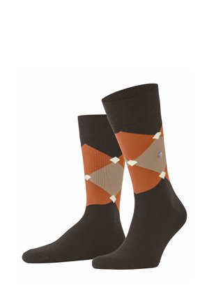 Par de calcetines marrón oscuro con patrón de diamantes argyle en naranja, beige y blanco en las pantorrillas, de pie sobre un fondo blanco.