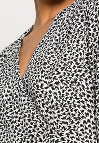 Svart och vit mönstrad tyg med zigzag-design, med en v-ringning och draperad textur. Tyget verkar slätt och lätt.