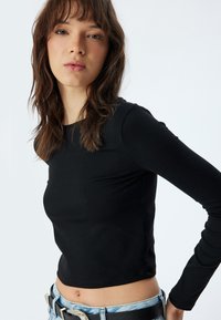 Zwarte lange mouwen aangesloten top gemaakt van rekbaar materiaal, met een ronde halslijn en een soepele textuur, gecombineerd met high-waisted denim.
