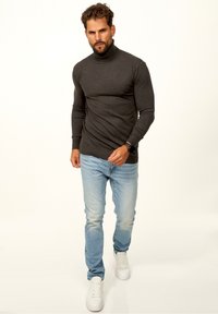 Schwarzer Rollkragenpullover mit gerippten Bündchen, kombiniert mit hellblauen Jeans und weißen Sneakers. Die Passform ist schmal und tailliert.