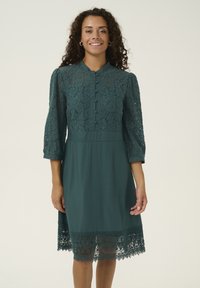 Abito in pizzo teal con maniche a tre quarti, chiusura a bottoni e motivo floreale. Presenta un intricata rifinitura in pizzo all'orlo e un corpetto texturizzato.