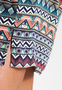 Mönstrad tyg i flera färger som visar geometriska mönster i teal, korall och marinblått, med en sidöppning och kantad kant.