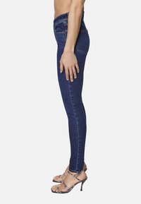 Smala jeans i mörkblå denim med midja som sitter på höften. Har en sidoficka, diskret sömnad och en slät yta. Stylad med strapponhögklackade skor.