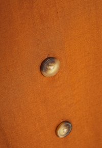Tessuto di lino arancione con una superficie texturizzata, caratterizzato da un grande bottone rotondo marrone cucito sul lato. Design semplice e pulito.