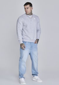 Světle šedá mikina s kulatým výstřihem, žebrovanými manžetami a lemem; v kombinaci se světle modrými d�žínami. Bílé tenisky dotvářejí celkový vzhled.