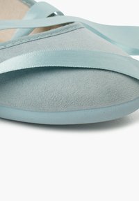 Light blue ballet flat made of soft suede. Features a flat toe, thin ribbons for wrap-around ties, and a smooth rubber sole.