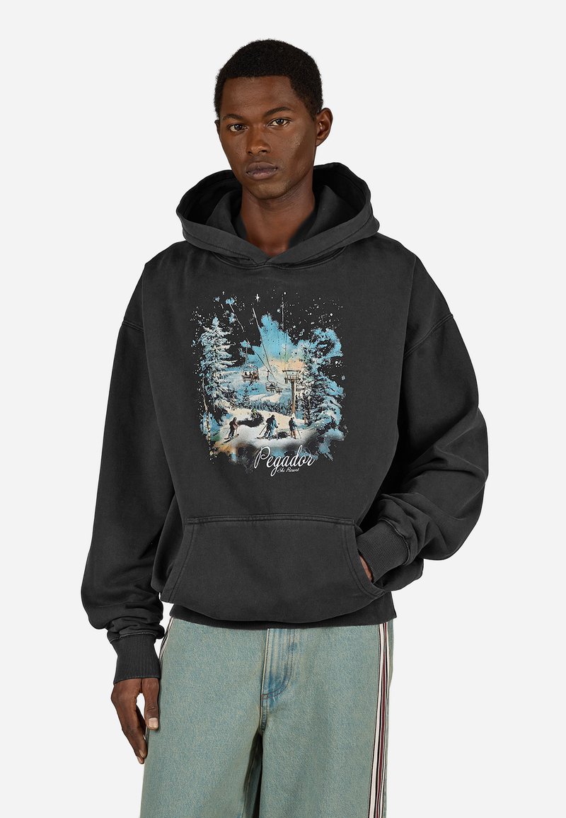 Μαύρη κο�υκούλα με μεγάλη μπροστινή γραφική απεικόνιση ενός χιονισμένου τοπίου και σκιέρ. Διαθέτει τσέπη καγκουρό και ριμπ μανσέτες.