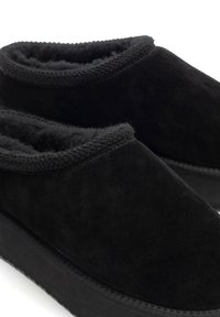 Černé semišové nazouvací boty s měkkým vnitřkem, zaobleným vrchem a silnou gumovou podrážkou. Mají měkký, texturovaný okraj pro pohodlí.