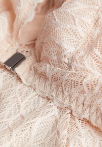 Lace top in zachte perzik met ingewikkelde, bladvormige patronen en een gladde, zilveren hardwareaccent. Gelaagd en textuurdesign.