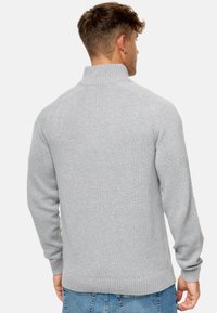 Suéter gris de punto con un alto cuello, puños acanalados y dobladillo. Presenta un patrón texturizado, una silueta ajustada y mangas raglán.