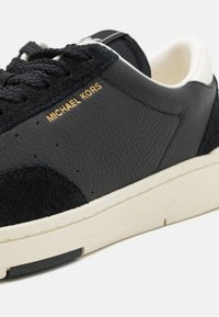 Mustad nahast spordijalanõud peene sametkattega, millel on tekstureeritud ülemine osa, valge vaheosa ja kuldne "MICHAEL KORS" bränding külgedel.