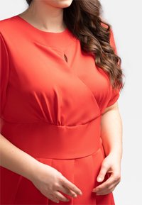 Červené šaty s krátkými rukávy, kulatým výstřihem s klíčovou dírkou, nařasením v pase a skládáním sukně.