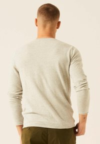 Lichtgrijze lange mouw shirt met een ronde hals, gemaakt van textuurstof, aansluitend bij de schouders en losjes bij de taille.
