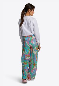 Witte blouse met geplooide kraag, gecombineerd met kleurrijke, gestreepte wijde broek in levendige tinten roze, teal en oranje.