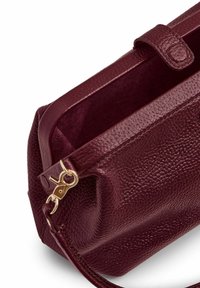 Vyno raudonos odos maišas su tekstūruotu paviršiumi. Yra auksinės spalvos užsegimas ir siuvinėta petneša. Atidaromas viršuje patogiam prisijungimui.