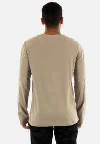 T-shirt a maniche lunghe color taupe realizzato in tessuto morbido; presenta un colletto rotondo e una vestibilità rilassata, indossato con pantaloni neri.