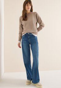 Beżowy prążkowany sweter nałożony na białą koszulę, w połączeniu z niebieskimi dzwonami jeansowymi i kremowymi trampkami. Prosty krój o swobodnym fasonie.