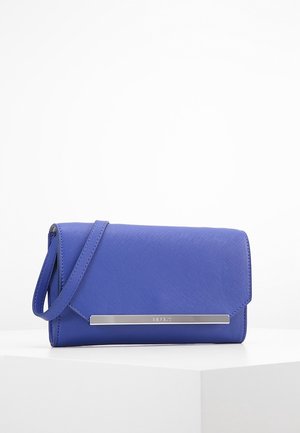 Pochette bracelet bleue à surface texturée, fermeture à rabat et détail en barre métallique argentée sur le devant, posée sur une surface blanche.
