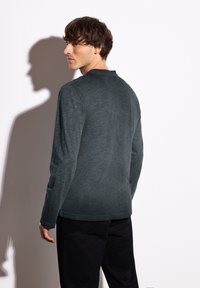 Herren Langarmhemd in Dunkelgrau, aus strukturiertem Stoff. Verfügt über einen Rundhalsausschnitt und eine leicht lockere Passform. Schwarze Hosen sichtbar.