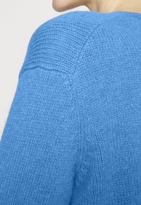Maglione azzurro lavorato a maglia che mostra una texture morbida con dettaglio a coste sulle spalle, caratterizzato da una vestibilità rilassata e un tessuto leggero.