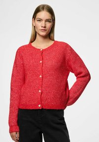 Stickad röd kofta med ett mönster av textur, rund halsringning och pärlknappar fram. Långa ärmar med ribbade manschetter.