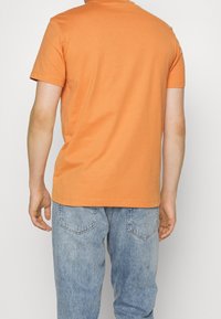 Oranžové bavlněné tričko s krátkými rukávy, kulatým výstřihem a běžným střihem, nošené s lehce modrými džíny z denimu s klasickým designem kapes.