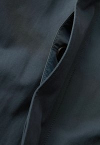 Mørkeblå stof med en glat tekstur, en knapdetalje og en delvist åben lomme, der afslører en lysere foder.