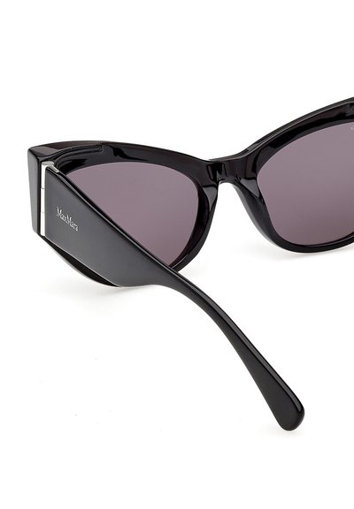Lunettes de soleil noires à monture œil de chat avec des verres foncés et des branches brillantes, ornées d'un logo de marque argenté sur la branche.