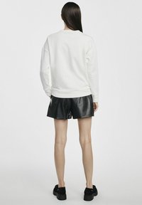 Biała bluza z opuszczonymi ramionami, ribbedowe mankiety i dół, zestawiona z czarnymi skórzanymi szortami. Gładka tekstura i luźny krój.
